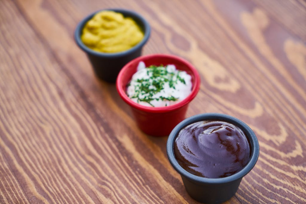 A close-up of three sauces in cups on a wooden surface, arranged in line.