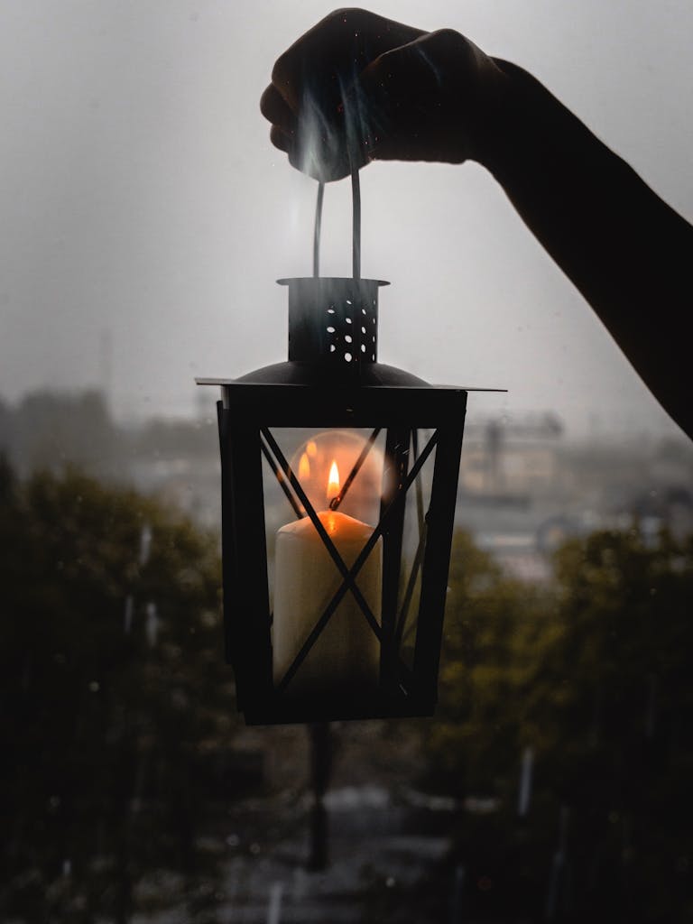 A glowing candle lantern held up against a rainy night backdrop, creating a moody ambiance.